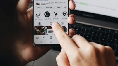 A person holding a cell phone in front of a laptop