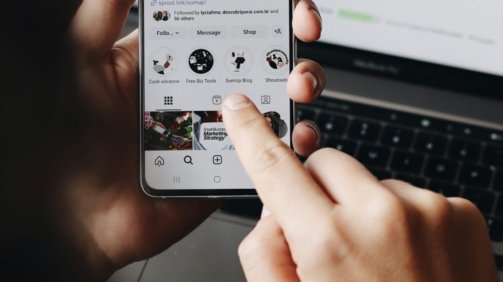 A person holding a cell phone in front of a laptop