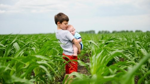 a young boy holding a baby in a field