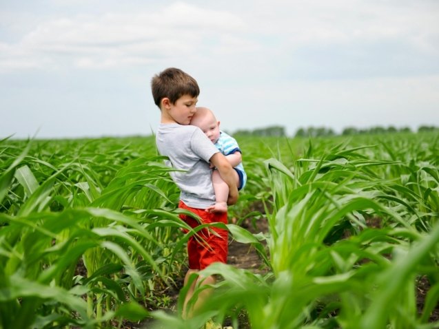 a young boy holding a baby in a field