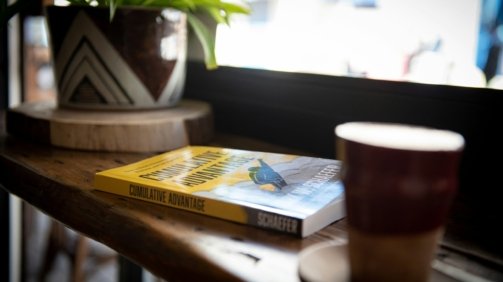blue and yellow book beside brown ceramic mug on brown wooden table