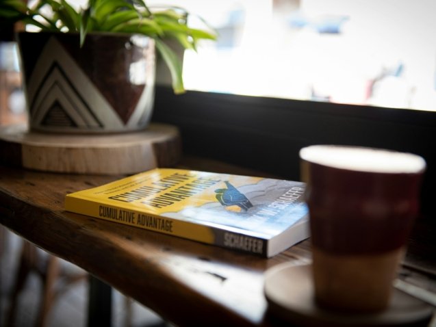 blue and yellow book beside brown ceramic mug on brown wooden table