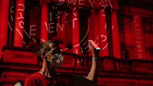 man in white crew neck t-shirt wearing black goggles standing near red building during nighttime