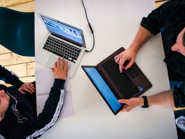 two men sitting at a table working on laptops