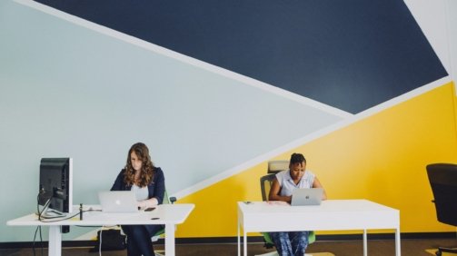 two women sitting beside table using MacBooks
